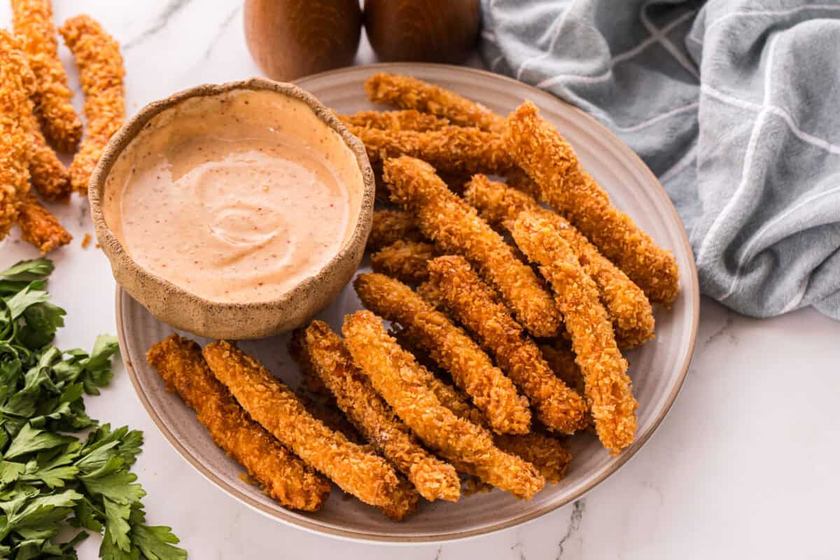 Overhead view of crispy chicken fries on a plate with a bowl of dipping sauce, garnished with fresh parsley.