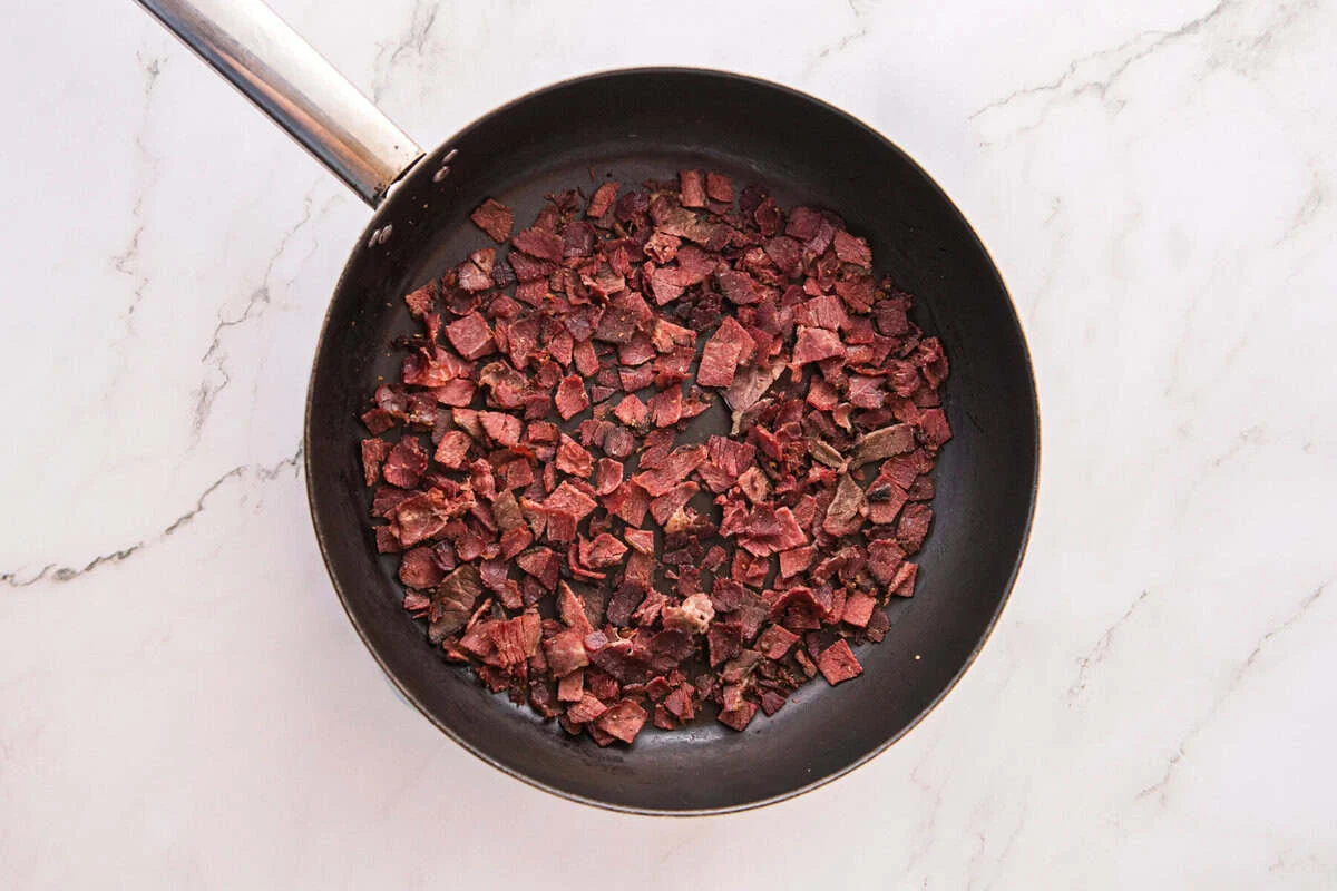 Chopped corned beef browning and crisping in a black skillet, ready to mix into the filling.