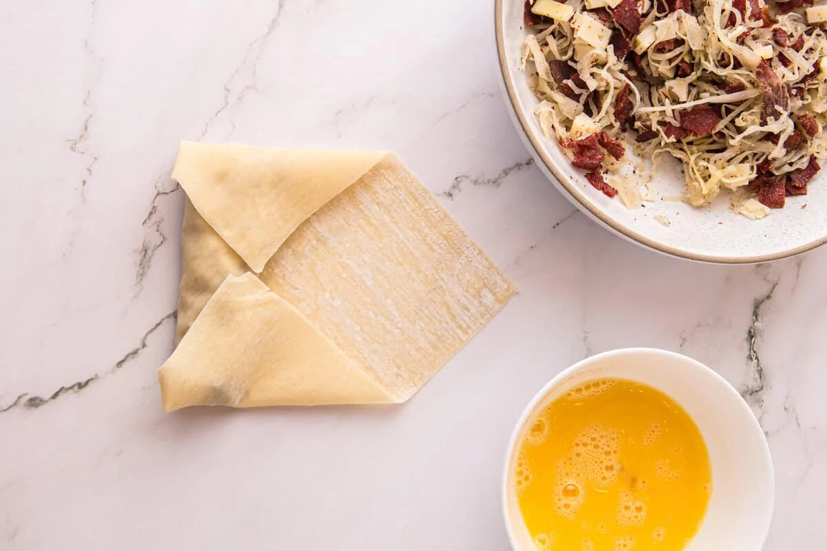 Egg roll wrapper folded envelope-style over the corned beef and sauerkraut filling before rolling tight.