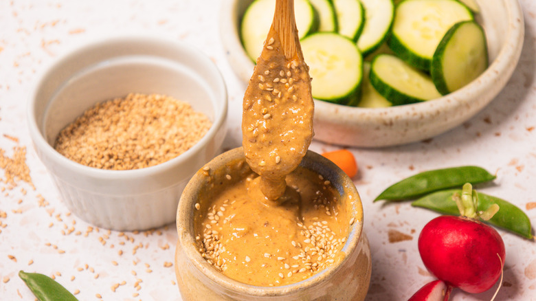 Dripping sesame dressing in small bowl with vegetables all around.