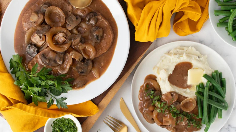 Slow-cooked steak and mushroom gravy on a plate with mashed potatoes and green beans