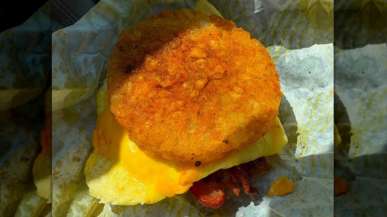 An egg, cheese, and bacon breakfast sandwich with a crispy hash brown for a bun sitting on paper