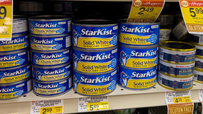 Cans of different kinds of StarKist brand tuna on a grocery store shelf.