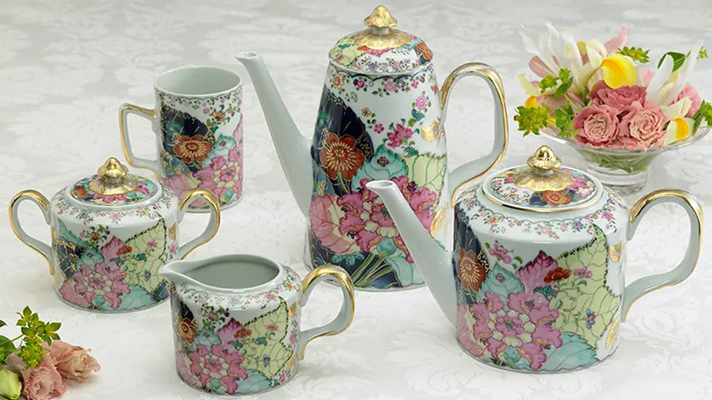A Tobacco Leaf  tea set from Mottahedeh featuring two elegant teapots, a milk jug, a mug and a sugar bowl on a lace tablecloth.