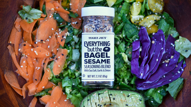 A bottle of Everything But The Bagel Sesame Seasoning Blend sits in a bowl filled with salad that's been sprinkled with the mixture
