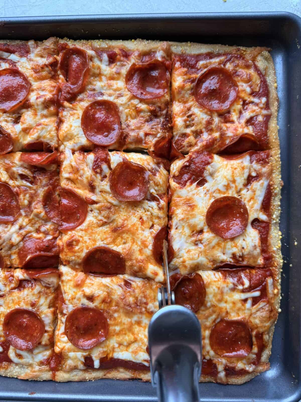 Close-up of a pizza cutter slicing the baked sheet pan pizza into squares