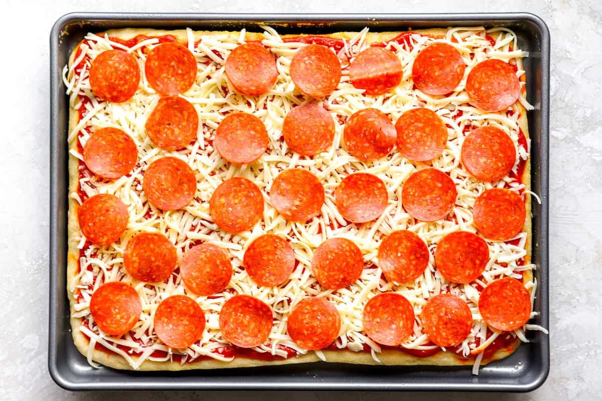 Unbaked sheet pan pizza topped with shredded mozzarella and pepperoni slices, ready for the oven