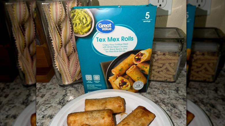 A box of Great Value brand Tex-Mex rolls sitting on a kitchen counter in front of pasta jars with the cooked rolls on a plate