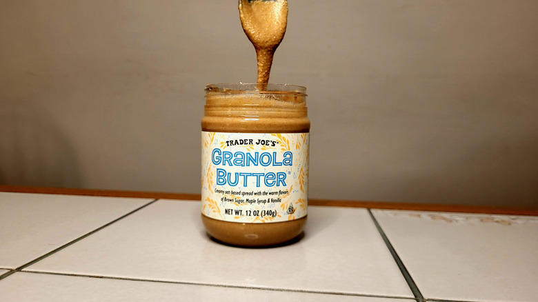 Granola butter is drizzled from a spoon back into the jar on a table.