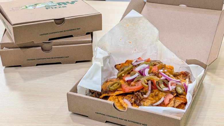 One open box of Doritos Hot Honey Nachos with steak next to two closed, stacked boxes on a light wood table