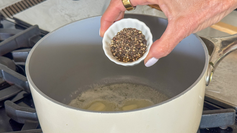 hand adding black pepper to pot