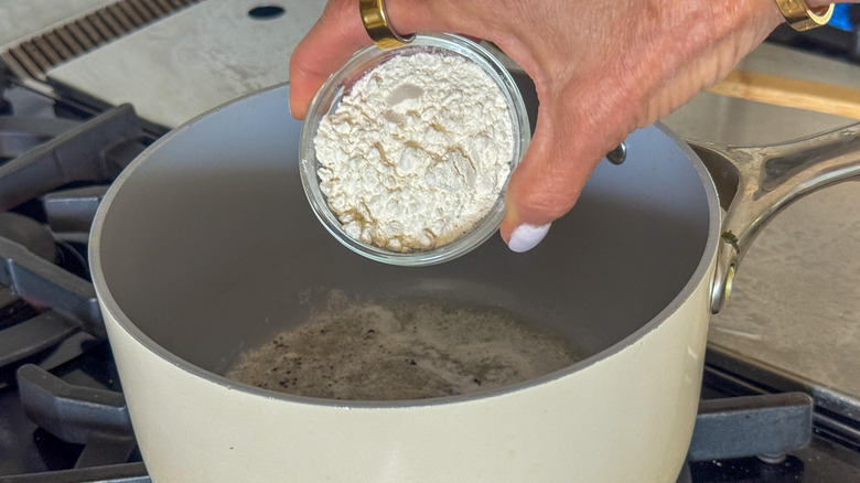 hand adding flour to pot