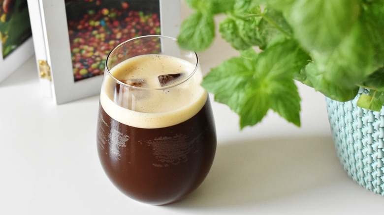 Nitro cold brew coffee in a glass on a white table with a plant in the background.