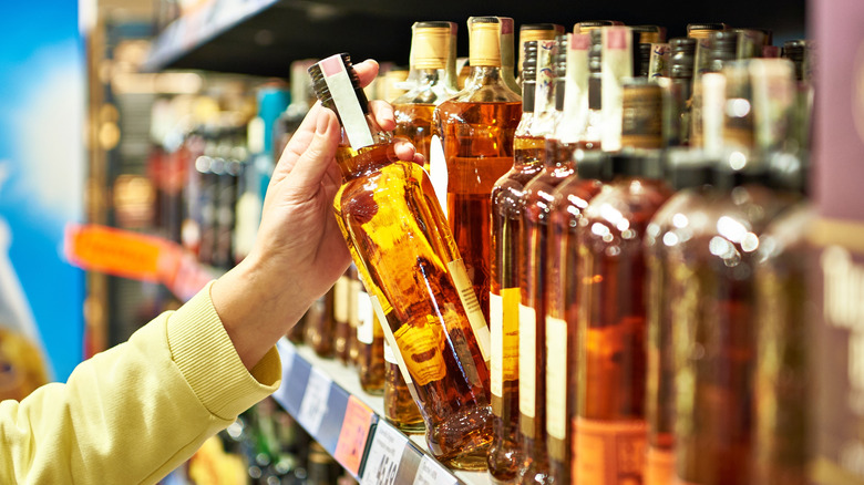 A person selecting a bottle of whiskey from a store shelf.