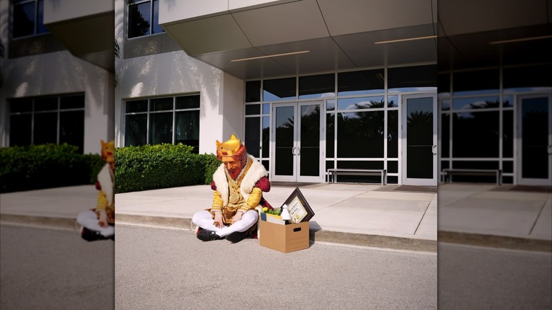 Burger King mascot sitting outside building with cardboard box of belongings