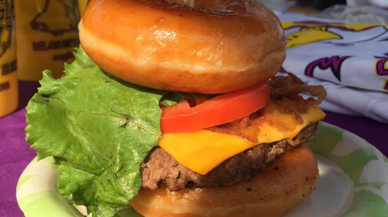 Burger on two donuts with cheese, lettuce, tomato, and bacon