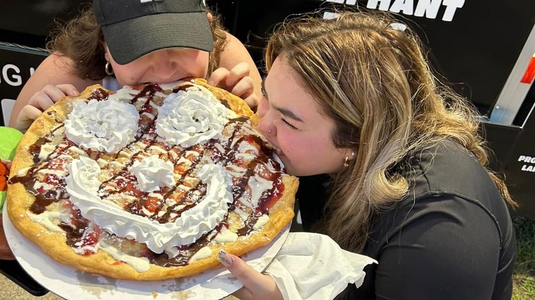 Two people sharing giant elephant ear with whipped cream siley face