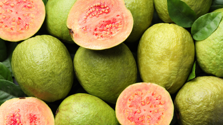A few guavas that have been sliced in half sit among a pile of whole guavas