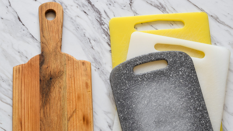 A wooden cutting board and three plastic cutting boards laying flat on a marble surface
