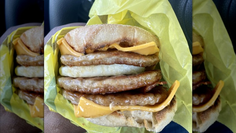 A person holding a Triple Stack McMuffin with sausage patties and two pieces of cheese