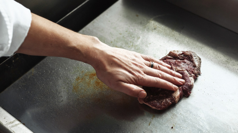hand pressing steak onto flat-top grill