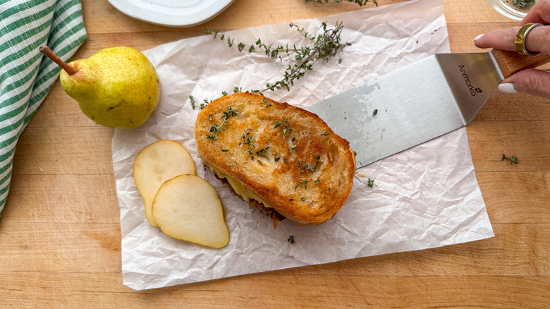 spatula placing sandwich on parchment paper next to pear