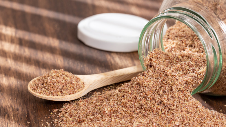 Ground flaxseed spilling from a glass jar.
