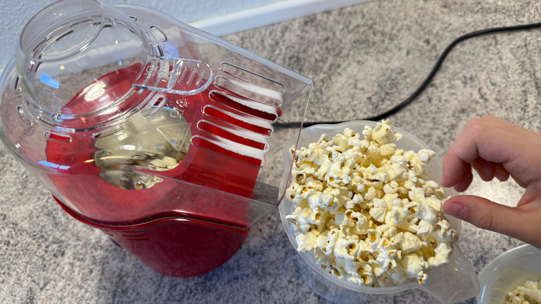 A hand picking freshly air-popped popcorn from a plastic jug