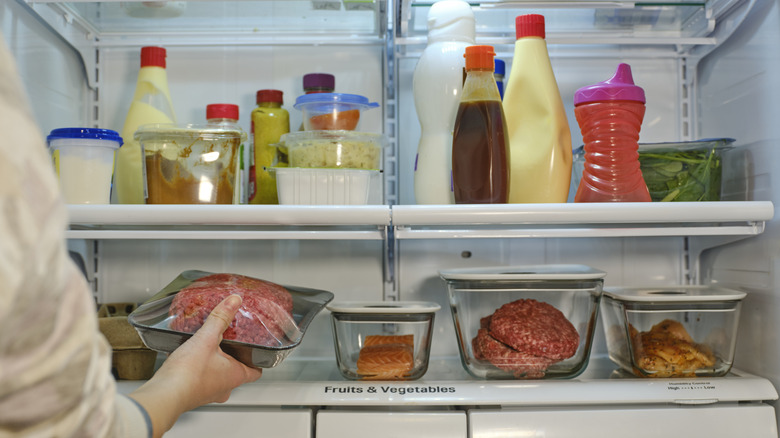 A person placing a wrapped package of meat in the bottom shelf of a refrigerator