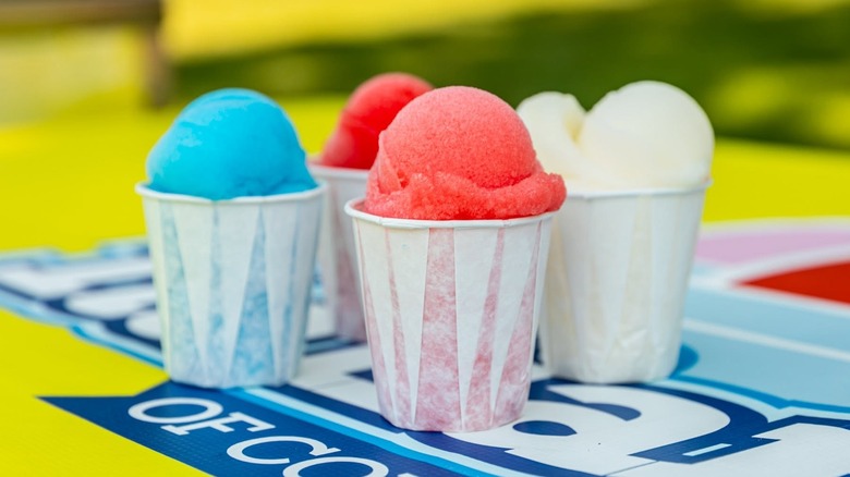Several flavors of Italian ice in cups atop a colorful banner