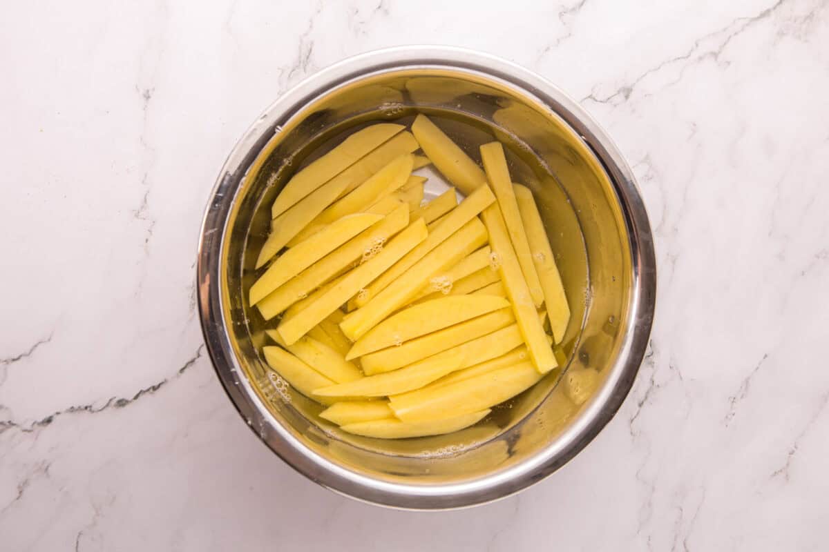 Cut russet potato fries soaking in a bowl of cold water to remove excess starch.