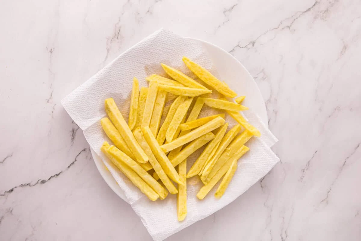 Soaked potatoes draining on a paper towel-lined plate before the first fry.