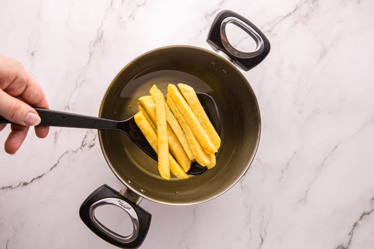 Golden double-fried potatoes being lifted out of the pot with a slotted spoon.
