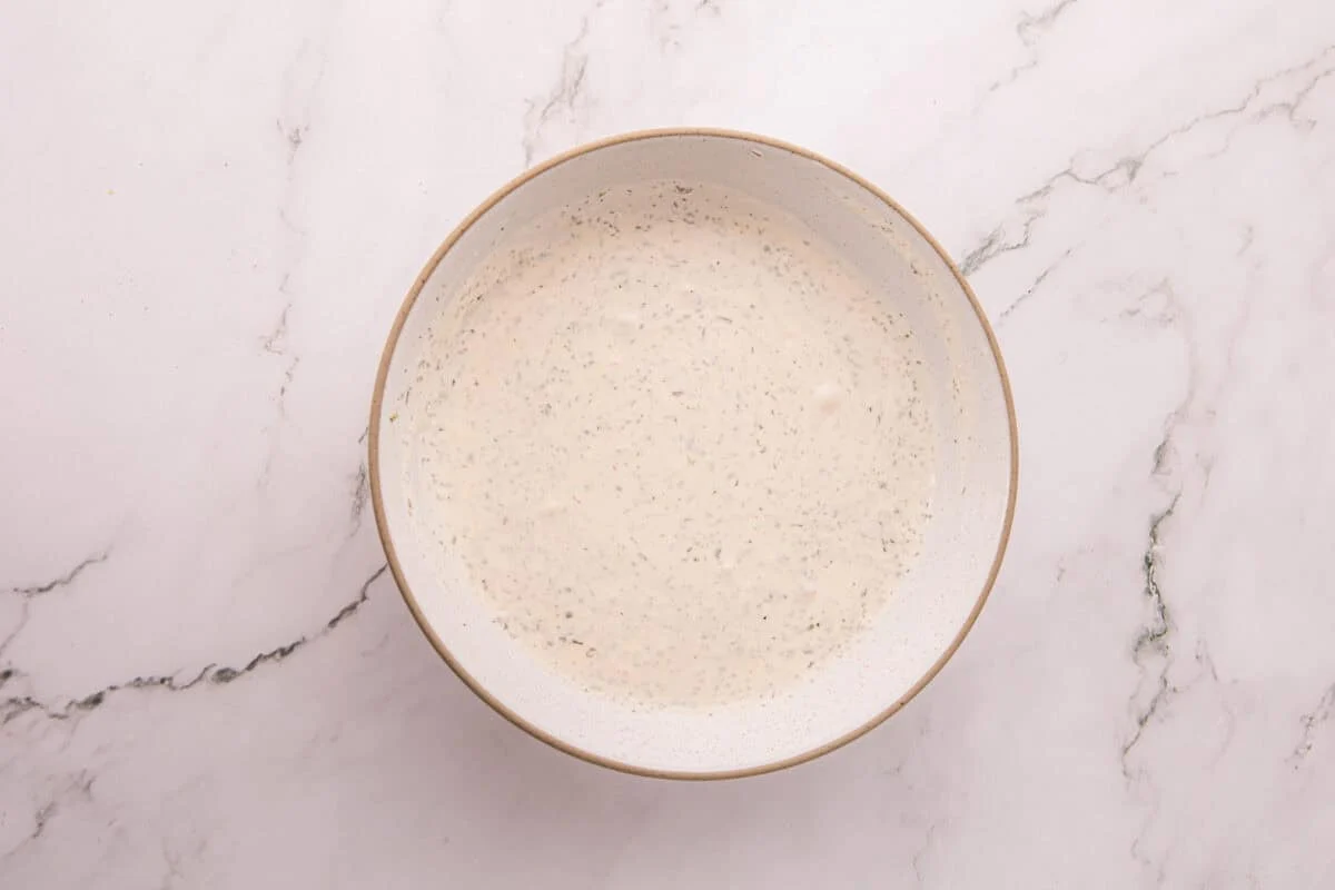 Homemade ranch dressing mixed in a bowl, flecked with dill and parsley.