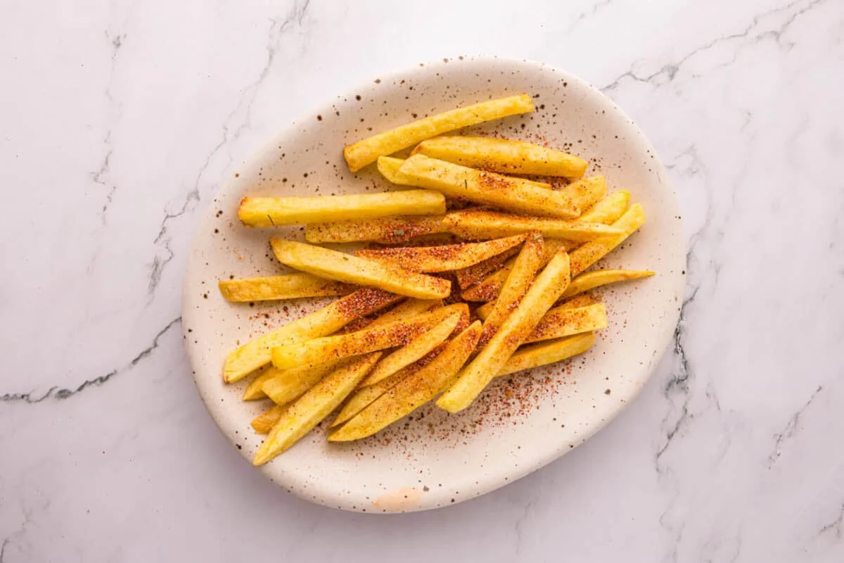 Crispy fries dusted with Cajun seasoning on a plate, before adding cheese sauce or ranch.