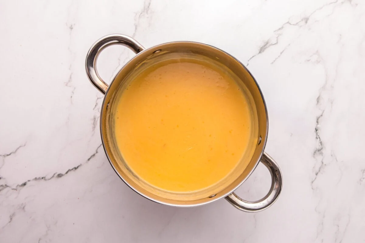 Smooth, glossy melted cheese sauce in a saucepan, ready to pour over the fries.