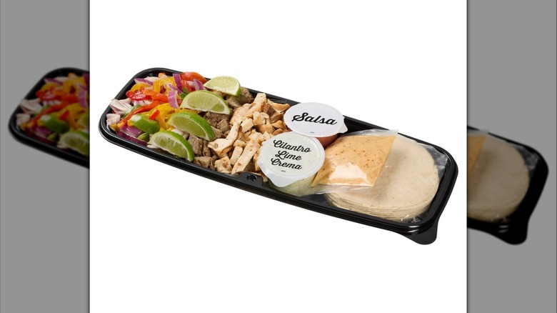 A Kirkland Signature Beef and Chicken Fajita Kit with meat, tortillas, sauces, vegetables, and lime wedges on display