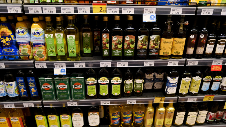 Several shelves in an Italian supermarket lined with bottles of various brands of olive oil.
