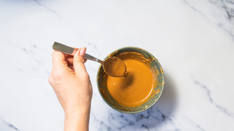 Lifting spoon of peanut sauce in bowl
