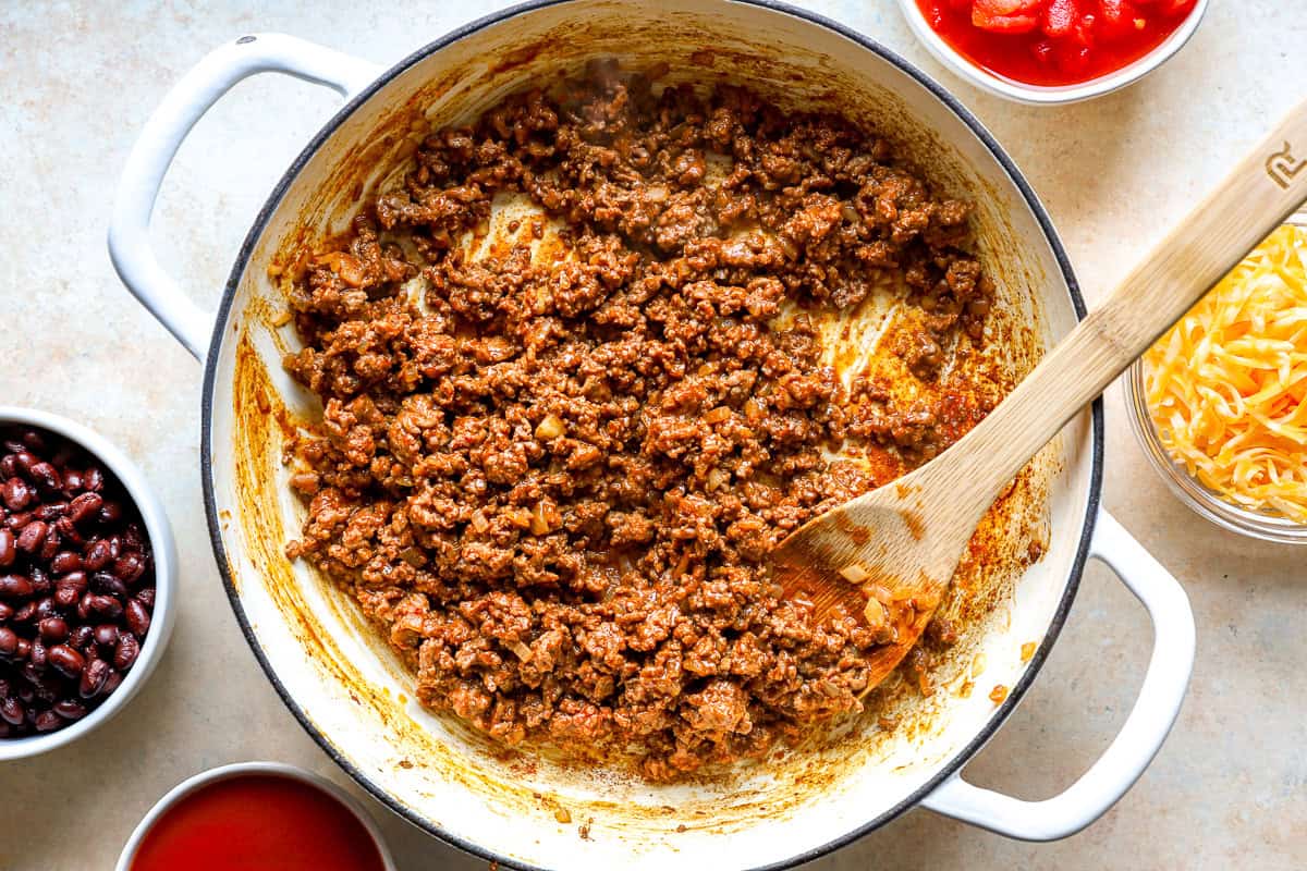 Browned ground beef with taco seasoning in a skillet, with bowls of black beans, diced tomatoes, and shredded cheese alongside.
