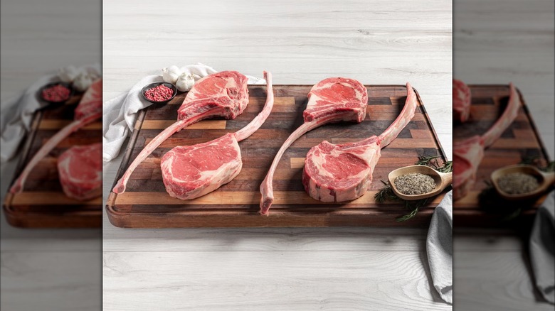 A shot of four Rastelli's Choice Black Angus Tomahawk Steaks on a wooden chopping block with spices and linen napkins.