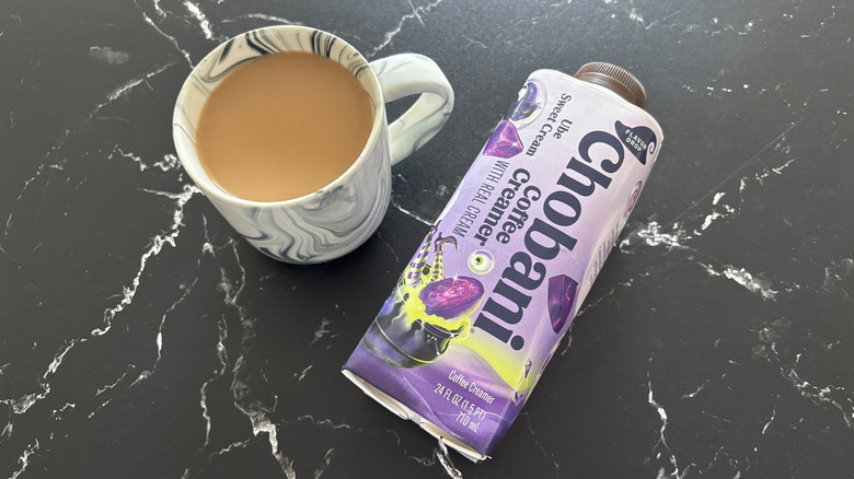 Cup of coffee in mug next to Chobani Ube Sweet Cream creamer bottle