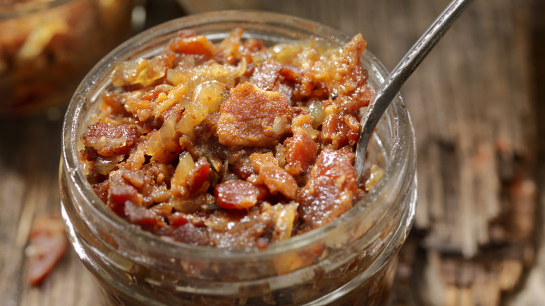 An open pot of bacon jam with a spoon in it sits on a table.