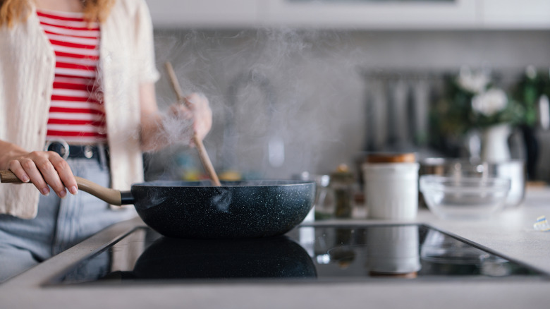 A woman stirring food as it cooks in a pan on an induction stove