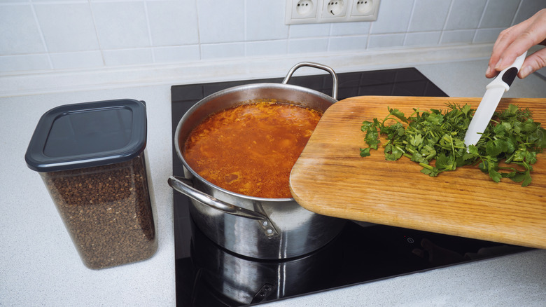 A woman adding chopped parsley to a pot of soup simmering on an induction cooktop