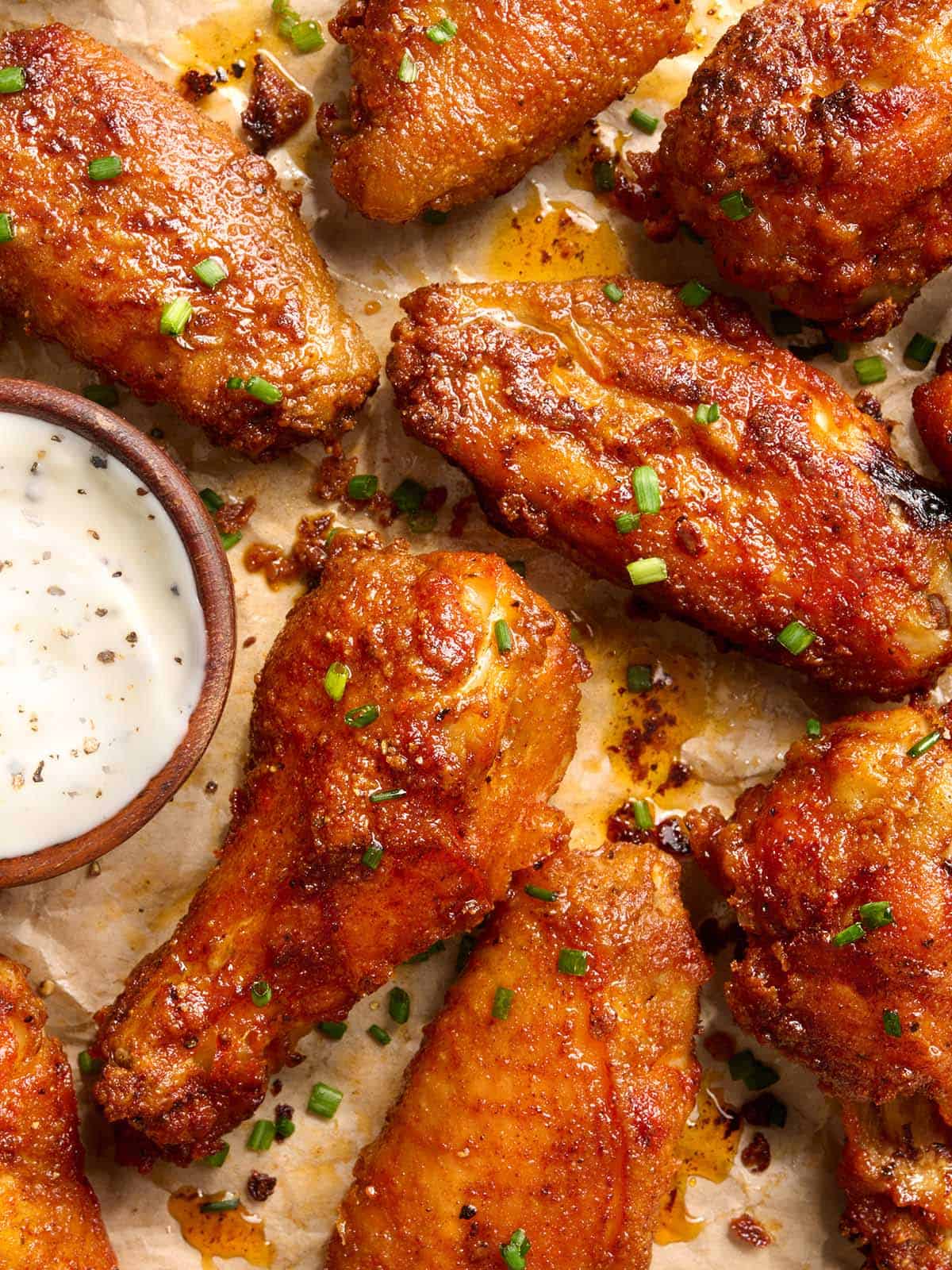 Overhead shot of crispy baked chicken wings on parchment paper with a small bowl of ranch dressing and fresh chives.