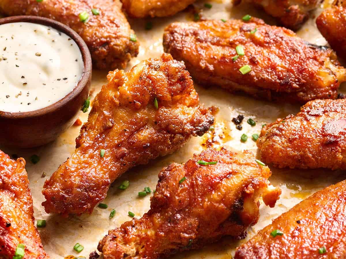 Close up of crispy baked chicken wings garnished with chives next to a bowl of ranch dressing.