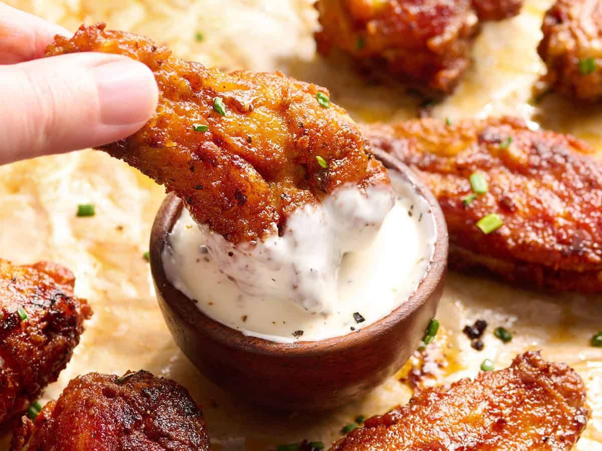 Hand dipping a crispy baked chicken wing into a bowl of creamy ranch dressing.