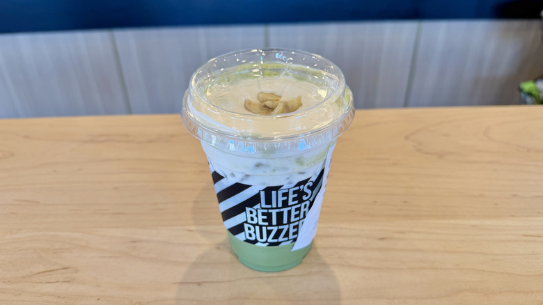 Better Buzz Banana Matcha in a plastic cup with banana chips on top on a wooden table
