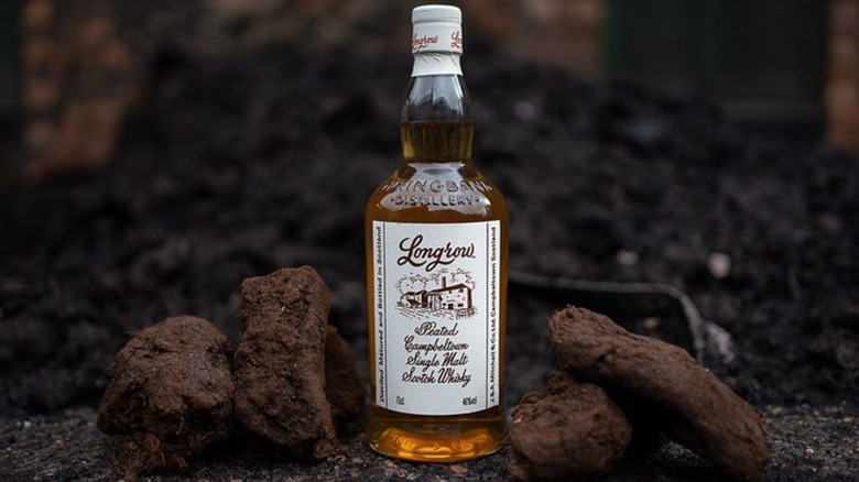 A bottle of Longrow Peated placed outside with a couple of lumps of peat either side